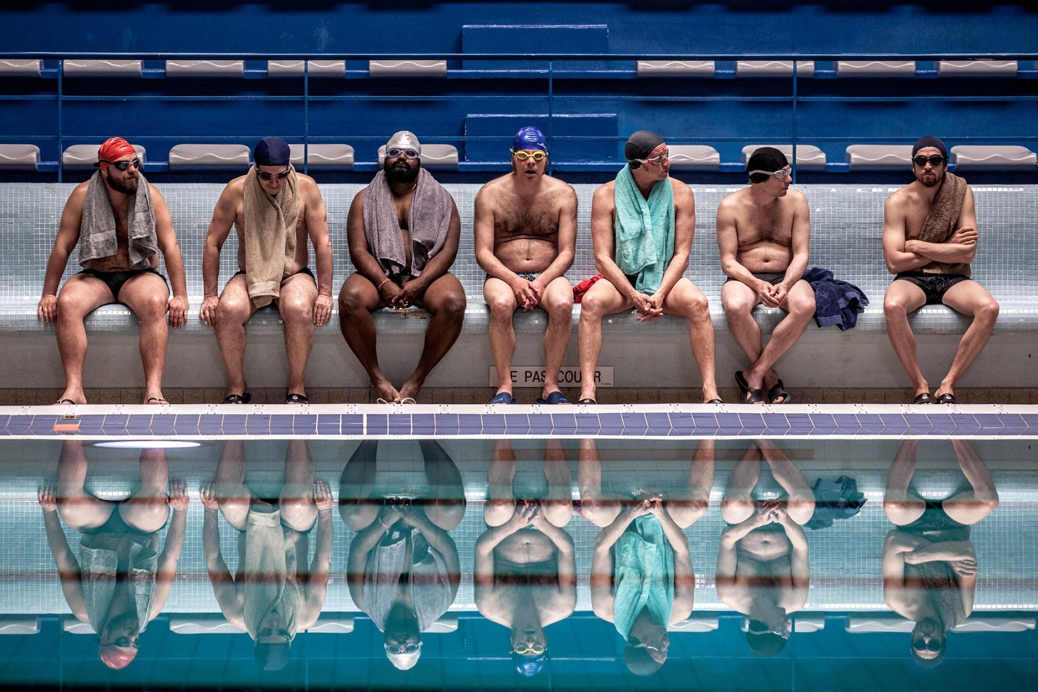 Siete hombres sentados en el borde de una piscina