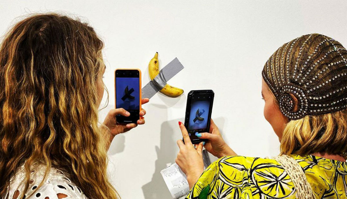 Dos mujeres fotografian la banana pegada en la pared